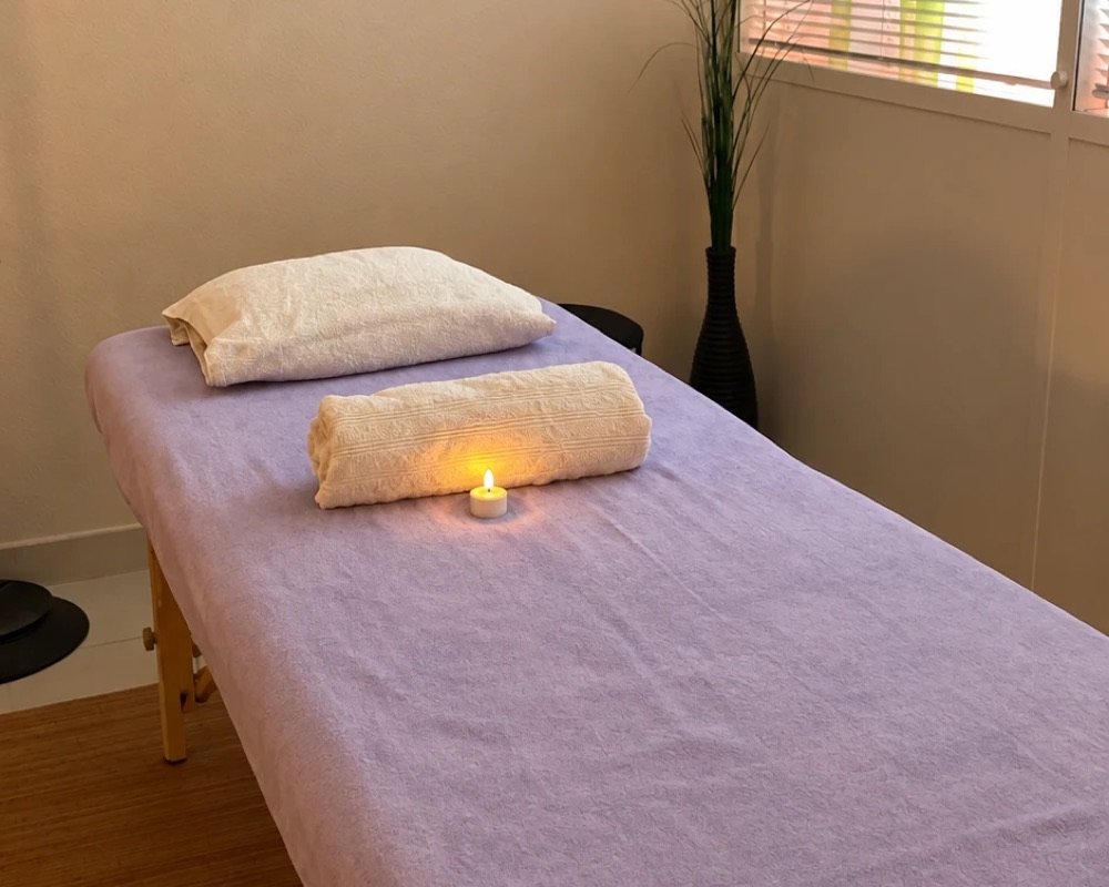 Table de massage installée pour un événement, avec coussin, serviette roulée et bougie allumée
